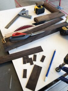 Woodworking tools and materials arranged on a work surface, including wood pieces and a pencil.