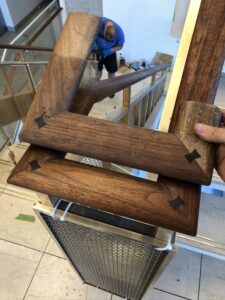 Wooden railing components are held above a metal mesh structure, with a worker in the background.