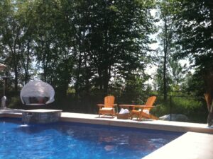 Bright outdoor pool scene featuring blue water, wooden chairs, and lush green trees.