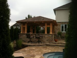Wooden gazebo with a stone base, surrounded by greenery and featuring seating areas.