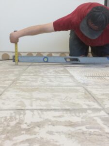 Person using a level and measuring tape to align tiles on a floor during installation.
