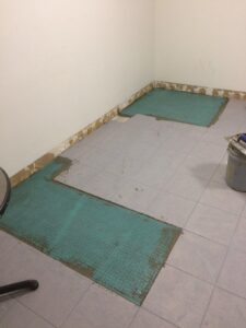 Bare room corner with partially tiled floor and green underlayment visible, construction in progress.