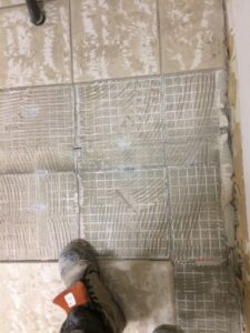 Tile flooring partially installed with adhesive and a worker’s boot in view.