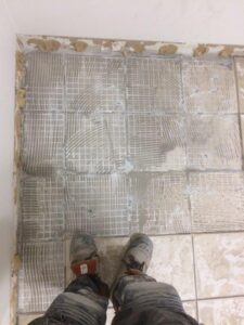 Feet in work boots standing on freshly laid tile adhesive with patterned surface.