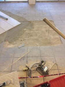 Tile floor under renovation with wet adhesive, tools, and loose wires scattered around.