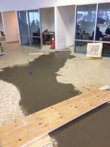 Newly poured gray concrete covers part of a tiled floor, with wooden planks for access.