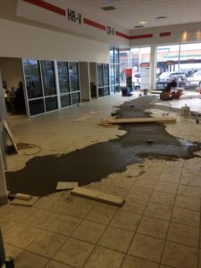 Construction area with partially poured concrete on a tiled floor and large windows in the background.
