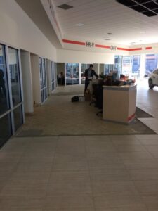Car dealership interior with reception area, employees working, and unfinished flooring.