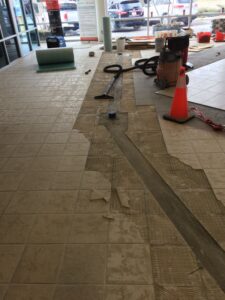Tiles are partially removed from a floor, revealing a construction area with tools and materials.