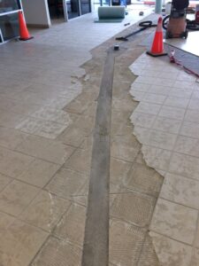 Uneven tile floor during renovation, exposing a concrete seam and construction materials nearby.