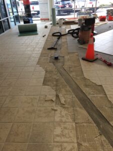 Floor being renovated with tiles removed, tools, and a caution cone in a commercial space.