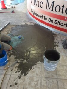 Freshly poured gray concrete is being smoothed on a tiled floor near a reception area.