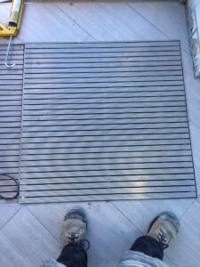 Feet in work boots stand above a gray striped mat on tiled flooring. Tools are nearby.