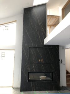 Tall black marble feature wall with gold veining and a fireplace opening, under construction.