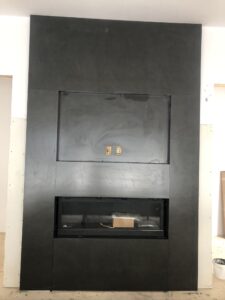 Modern black fireplace framed in textured panels, with electrical outlets above.