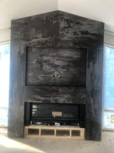 Modern fireplace installation with textured gray wall, framed opening, and unfinished wood base.