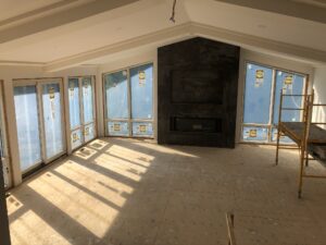 Spacious, unfinished living room with large windows, exposed beams, and a rustic fireplace.