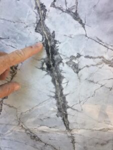 Hand pointing at a gray marble surface with visible veining and cracks.
