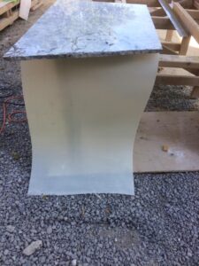 Granite countertop atop a curved beige base, placed on gravel at a construction site.