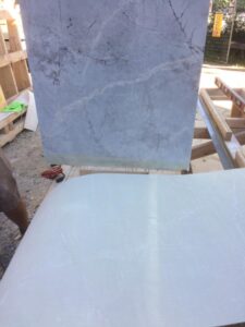 Gray marble slabs are positioned on a wooden surface, showcasing textured patterns and veins.