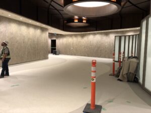 Construction area with a worker, curved floor, and orange safety cones along the walls.