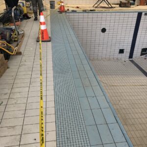 Under construction, empty swimming pool area with caution cones and worker equipment.